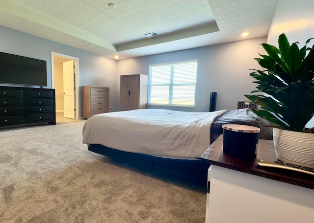 bedroom with visible vents, a textured ceiling, carpet, and a tray ceiling