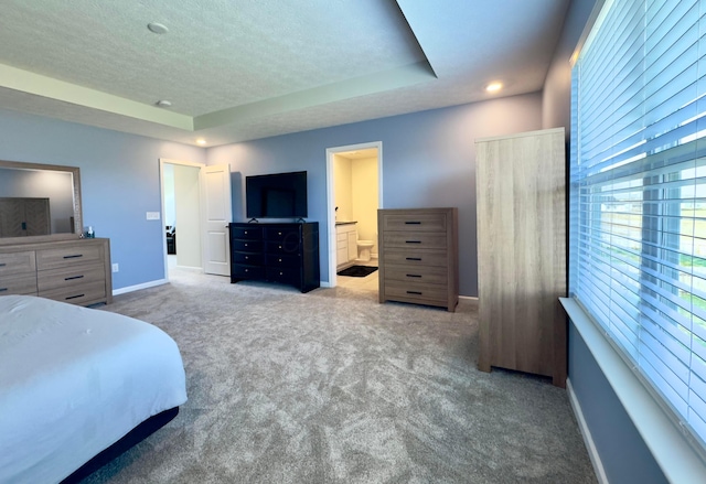 carpeted bedroom featuring a textured ceiling, baseboards, a raised ceiling, and ensuite bath
