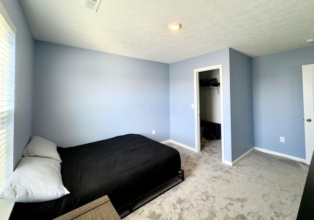 bedroom featuring carpet flooring, a textured ceiling, baseboards, a spacious closet, and visible vents