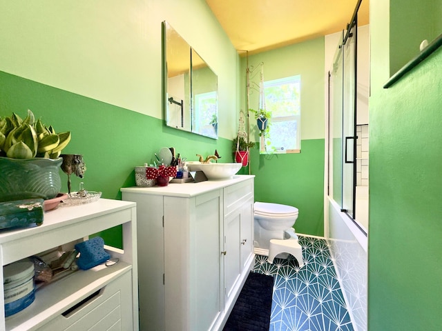 bathroom featuring toilet, baseboards, enclosed tub / shower combo, and vanity