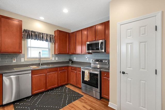 kitchen with dark countertops, a sink, light wood finished floors, appliances with stainless steel finishes, and backsplash