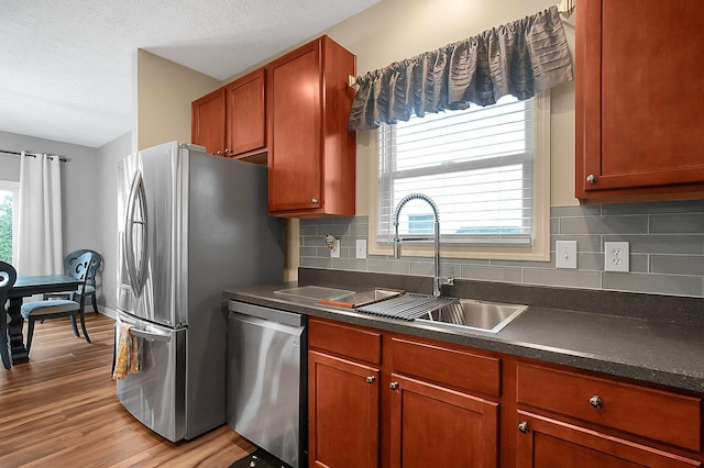 kitchen with decorative backsplash, dark countertops, light wood-style floors, a sink, and appliances with stainless steel finishes