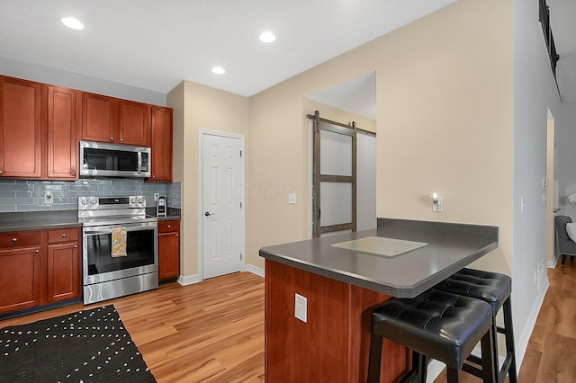 kitchen with dark countertops, a breakfast bar, a barn door, light wood-style floors, and stainless steel appliances