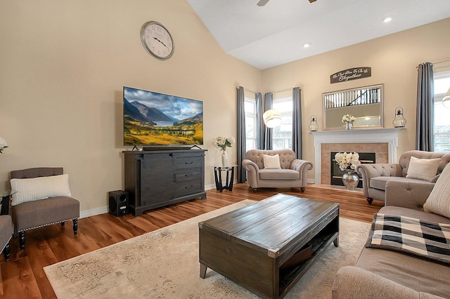 living room featuring ceiling fan, baseboards, wood finished floors, a tile fireplace, and vaulted ceiling