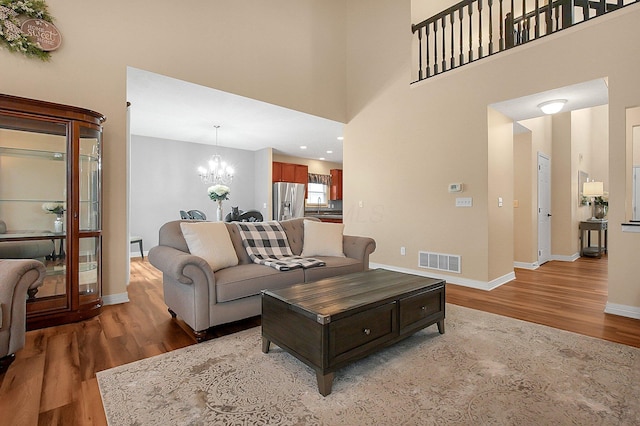 living area featuring a towering ceiling, visible vents, wood finished floors, baseboards, and a chandelier