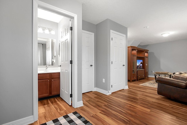 hall with a sink, baseboards, and light wood-style flooring