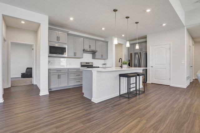 kitchen with decorative backsplash, dark wood-style flooring, a kitchen bar, gray cabinetry, and stainless steel appliances