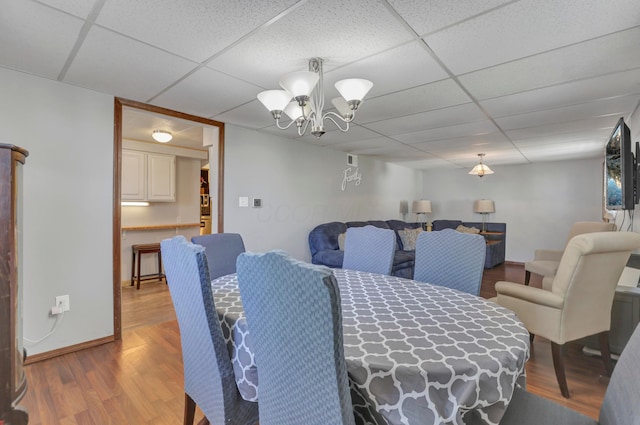 dining space featuring a paneled ceiling, baseboards, an inviting chandelier, and wood finished floors