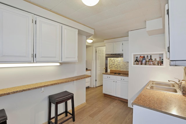 kitchen with a sink, light wood-style flooring, backsplash, and white cabinetry