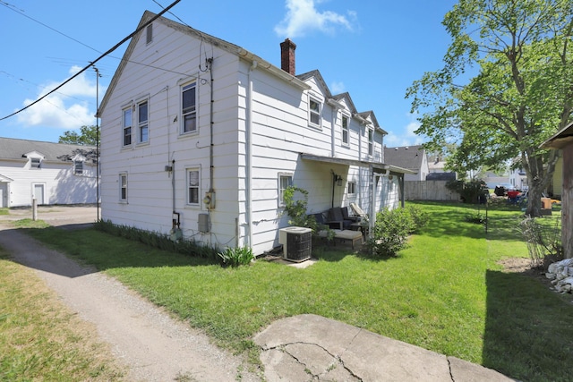 back of property with a lawn, fence, a chimney, and central AC