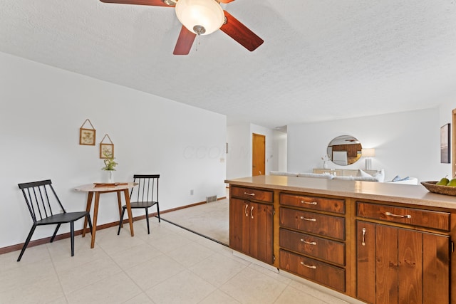 kitchen with a ceiling fan, a textured ceiling, light countertops, baseboards, and open floor plan