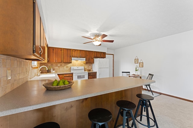 kitchen with a peninsula, white appliances, ceiling fan, under cabinet range hood, and a sink