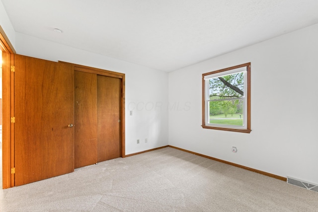 unfurnished bedroom featuring baseboards, a closet, light colored carpet, and visible vents