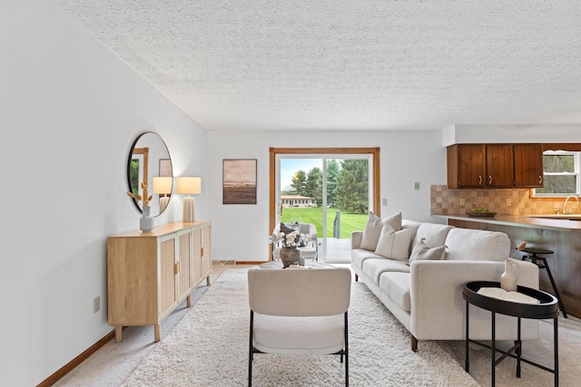 living room with baseboards, plenty of natural light, a textured ceiling, and light colored carpet