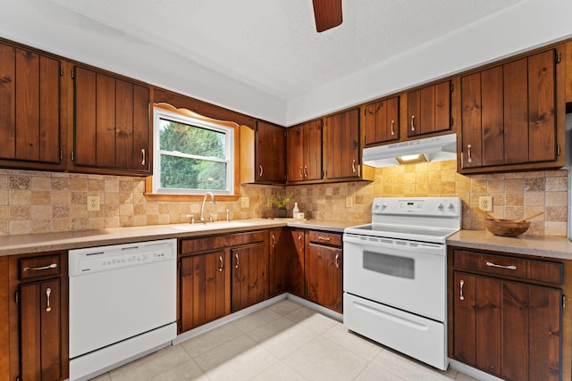 kitchen with a sink, white appliances, light countertops, decorative backsplash, and under cabinet range hood