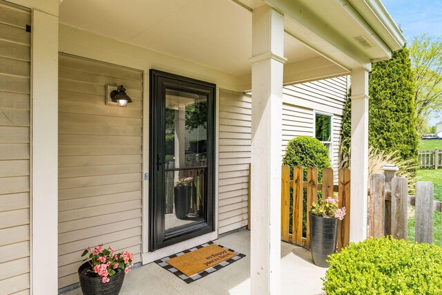 property entrance featuring a porch, fence, and visible vents
