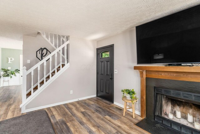 foyer with stairs, wood finished floors, a fireplace, baseboards, and a textured ceiling