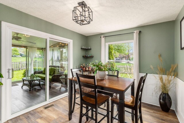 dining area with a textured ceiling, visible vents, wood finished floors, and an inviting chandelier