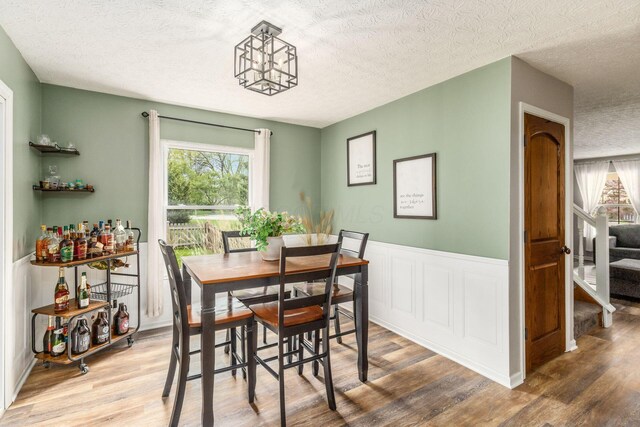 dining space featuring a healthy amount of sunlight, wainscoting, a textured ceiling, and wood finished floors