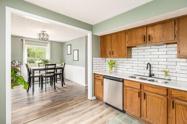 kitchen featuring stainless steel dishwasher, a sink, brown cabinetry, and light countertops