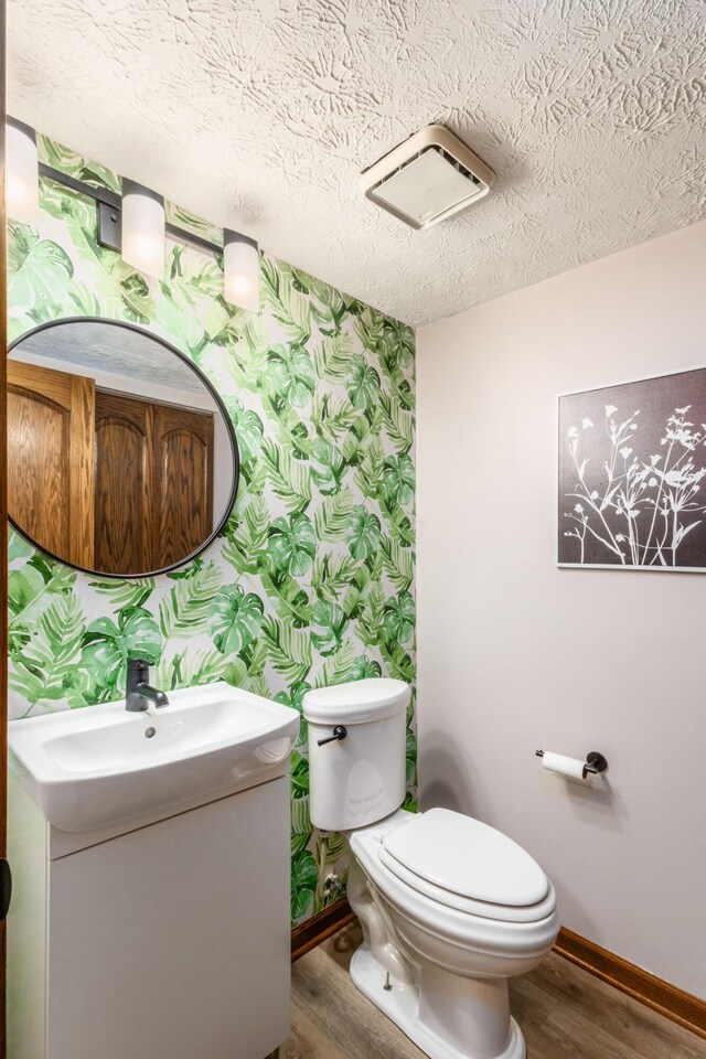 bathroom with baseboards, toilet, wallpapered walls, and wood finished floors
