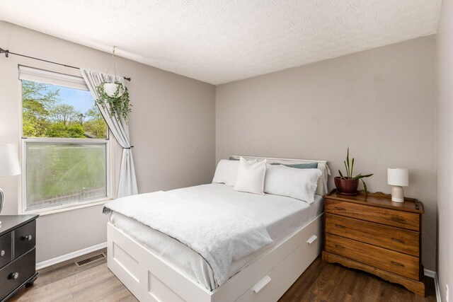 bedroom with baseboards, a textured ceiling, wood finished floors, and visible vents