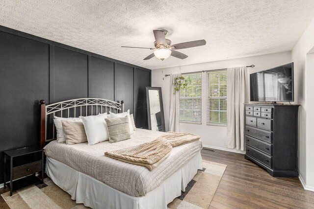bedroom featuring baseboards, a ceiling fan, a decorative wall, and wood finished floors