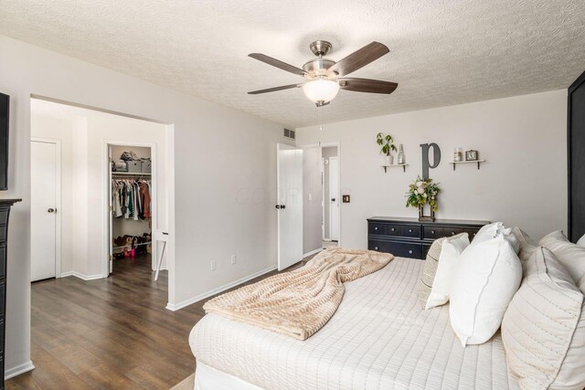 bedroom with a walk in closet, a textured ceiling, dark wood finished floors, visible vents, and a closet