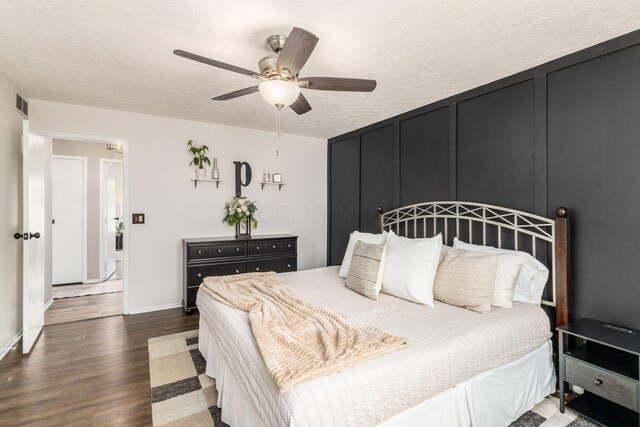 bedroom with ceiling fan, a textured ceiling, baseboards, wood finished floors, and visible vents