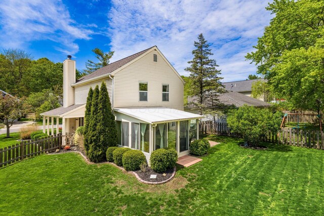 back of house with a lawn, a fenced backyard, a sunroom, and a chimney