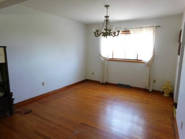 unfurnished dining area featuring visible vents, wood finished floors, and a chandelier