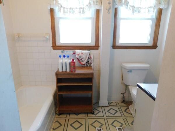 full bath featuring tile patterned flooring, vanity, toilet, a tub to relax in, and a notable chandelier