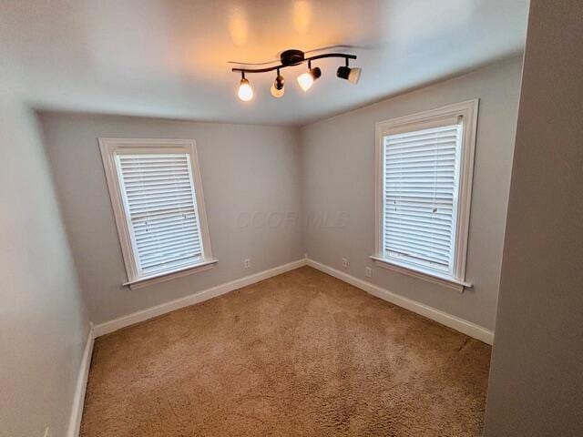 empty room featuring carpet floors, baseboards, and a healthy amount of sunlight