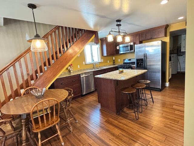 kitchen with appliances with stainless steel finishes, a breakfast bar area, wood finished floors, a kitchen island, and pendant lighting