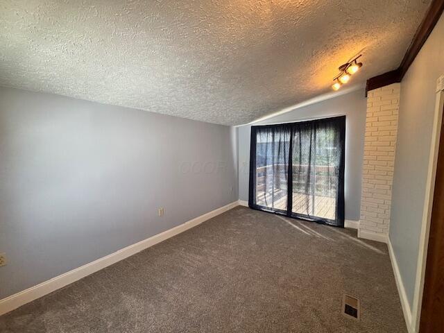 unfurnished room featuring baseboards, vaulted ceiling, dark colored carpet, and a textured ceiling