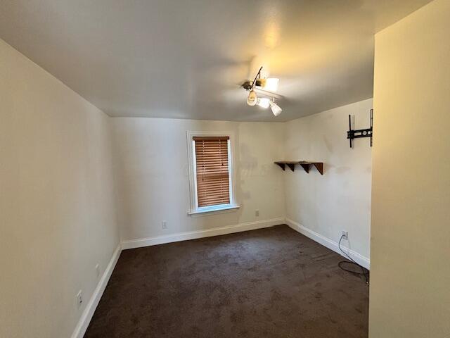 unfurnished room featuring baseboards and dark carpet