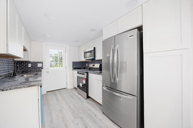 kitchen featuring backsplash, appliances with stainless steel finishes, dark countertops, light wood-type flooring, and a sink