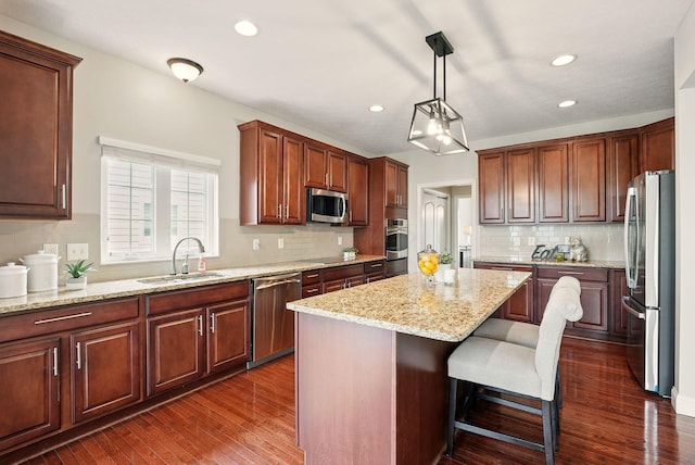 kitchen with a kitchen island, backsplash, dark wood finished floors, a sink, and stainless steel appliances
