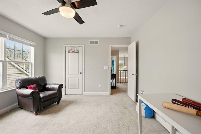 living area with baseboards, ceiling fan, visible vents, and light colored carpet