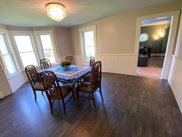 dining room featuring dark wood finished floors, a wainscoted wall, and a notable chandelier