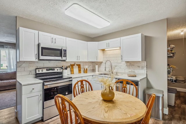 kitchen featuring a textured ceiling, appliances with stainless steel finishes, wood finished floors, light countertops, and a sink