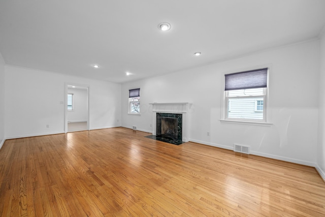 unfurnished living room featuring visible vents, a high end fireplace, light wood-style flooring, and a healthy amount of sunlight