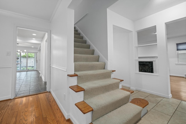 stairs featuring crown molding, baseboards, wood finished floors, and a fireplace