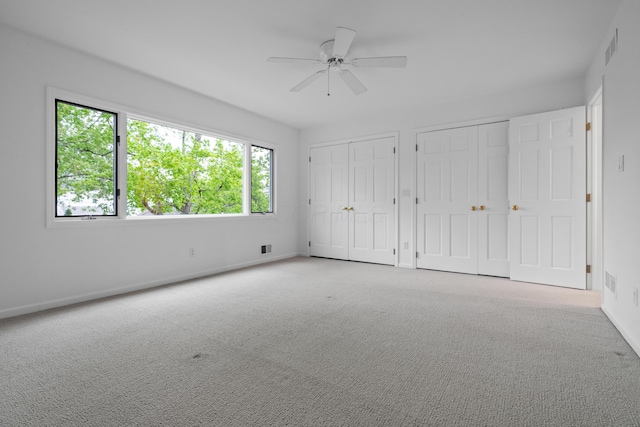 unfurnished bedroom with baseboards, carpet, two closets, and visible vents