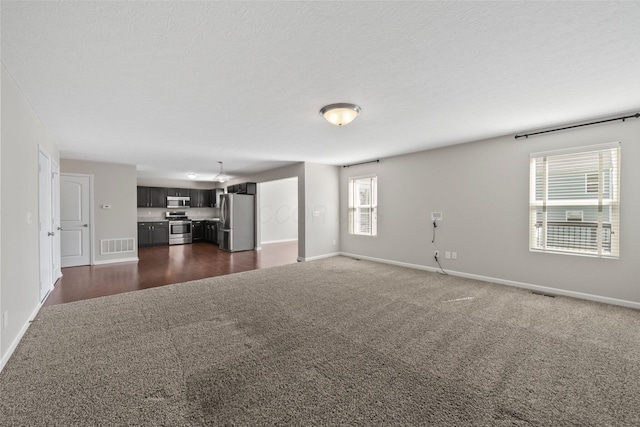 unfurnished living room featuring baseboards, dark carpet, and visible vents