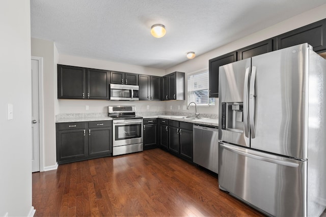 kitchen with a sink, light countertops, a textured ceiling, stainless steel appliances, and dark wood-style floors