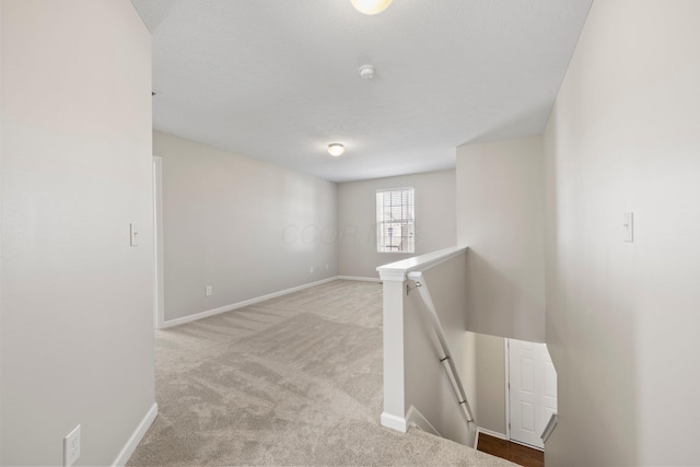 hallway featuring carpet floors, baseboards, and an upstairs landing
