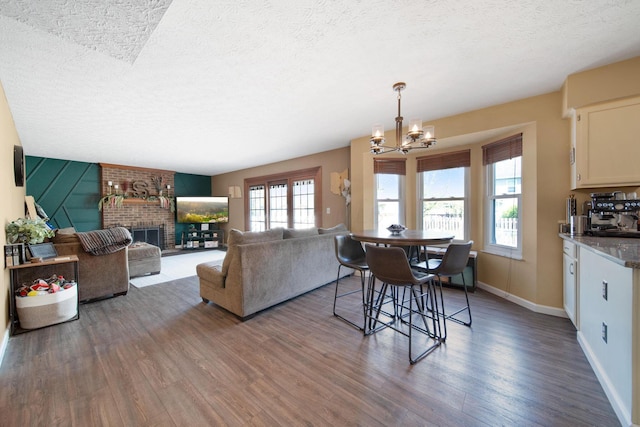 dining area featuring a brick fireplace, a textured ceiling, a chandelier, baseboards, and wood finished floors
