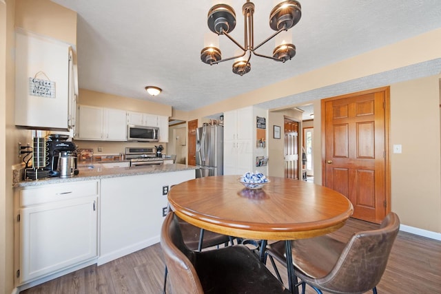 kitchen featuring light wood-style floors, a peninsula, an inviting chandelier, stainless steel appliances, and white cabinetry