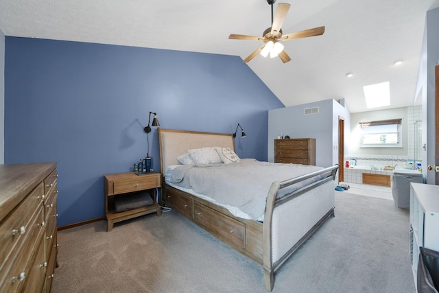 bedroom featuring visible vents, ensuite bathroom, ceiling fan, light colored carpet, and vaulted ceiling with skylight